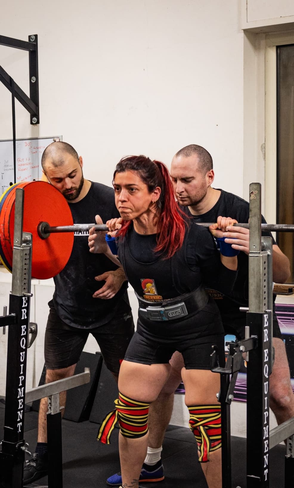 Atleta in squat con due compagni di squadra pronti a fare da spotter